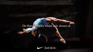 Gymnast in blue leaps mid-air; overlaid text: 'Do things history could only dream of.' Nike logo and 'Just do it.' below. Blurred background.